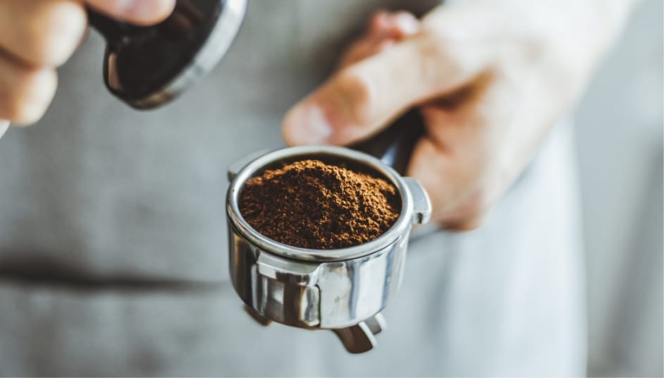 Person hält Siebträger mit frischem Kaffeepulver und Tamper in der Hand im Café
