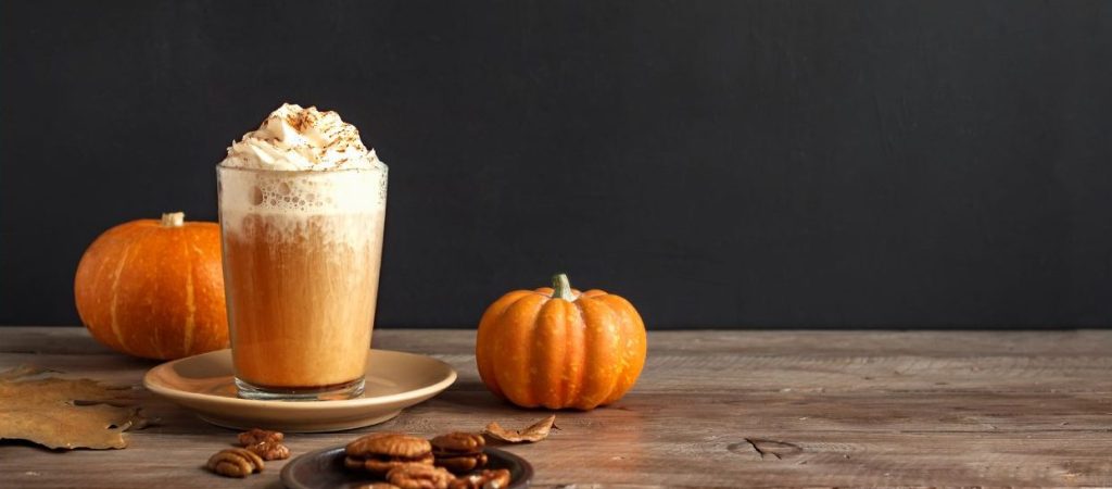 Ein cremiger Pumpkin Spice Latte steht neben einem frischen Kürbis – der perfekte herbstliche Genussmoment.