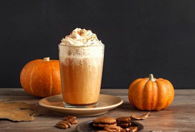 Ein cremiger Pumpkin Spice Latte steht neben einem frischen Kürbis – der perfekte herbstliche Genussmoment.