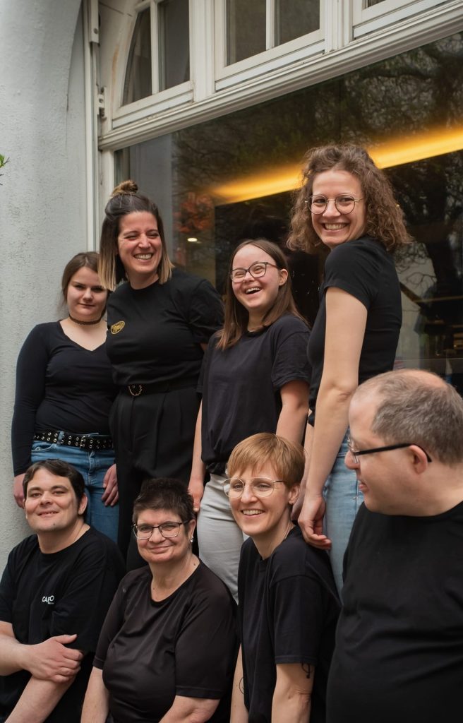 Das inklusive Team der Cafesito Kaffee Behindertenwerkstatt steht vor dem Café und zeigt, wie mit Leidenschaft und Teamgeist hochwertige Kaffeekreationen entstehen.