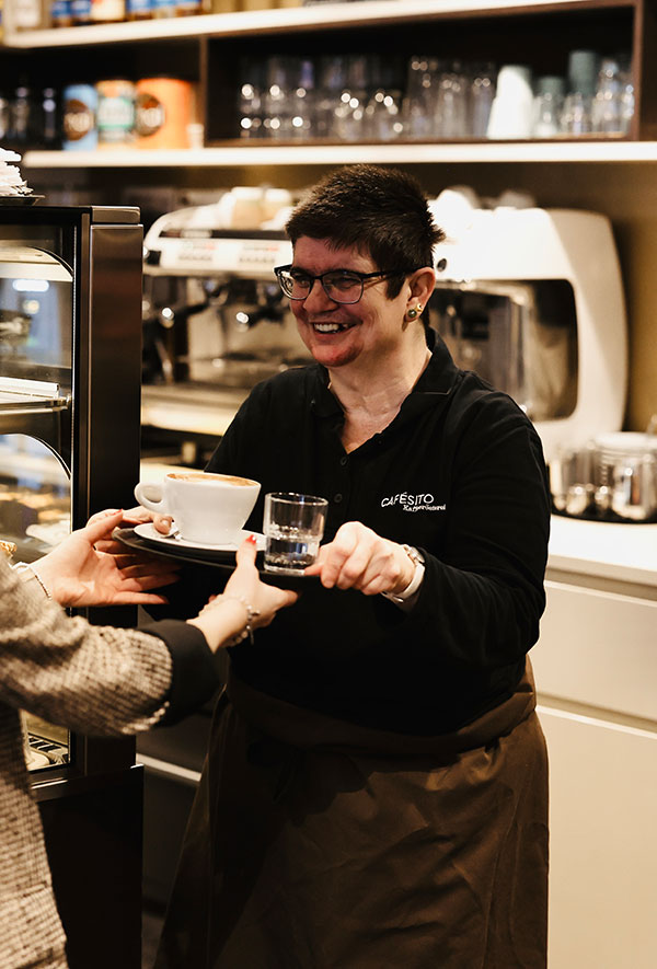 Barista in der Cafésito Kaffeerösterei serviert Kaffee mit einem Lächeln und erklärt Was ist Schümli Kaffee?